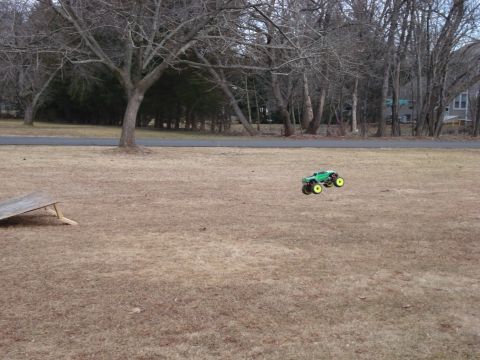 1994 Ford Bronco - A remote control monster truck is captured in mid-air, its bright green body and yellow wheels against a backdrop of trees.