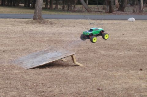 1994 Ford Bronco - A remote control monster truck performs a jump over a ramp in a grassy outdoor area.