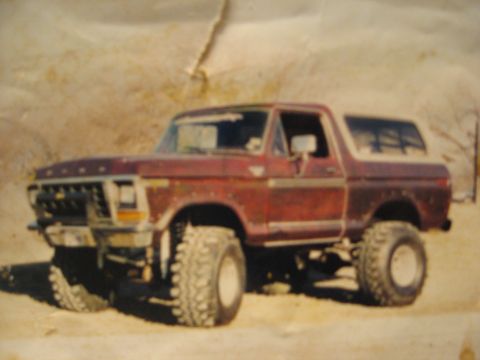 1979 Ford Bronco - A red Ford Bronco with a lifted suspension and oversized tires is parked outdoors.