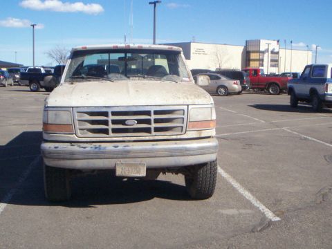 1992 Ford F-250 - A dirty white 1992 Ford F-250 pickup truck is parked in a lot under a bright sky.