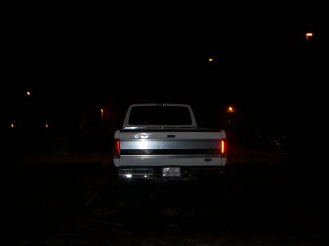 1992 Ford F-250 - The rear of a white 1992 Ford F-250 pickup truck is visible at night, with its taillights illuminated.