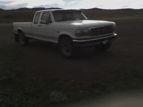 1992 Ford F-250 - A white 1992 Ford F-250 pickup truck is parked on a dirt lot with hills in the background.