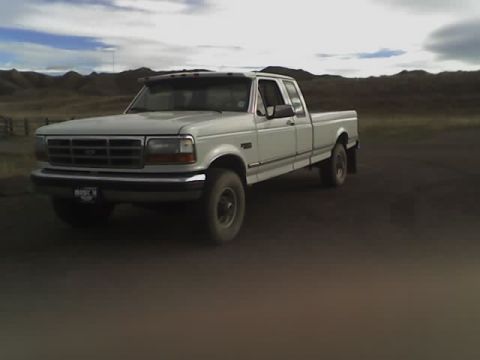 1992 Ford F-250 - A white 1992 Ford F-250 pickup truck is seen from a three-quarter front angle on a dirt road.