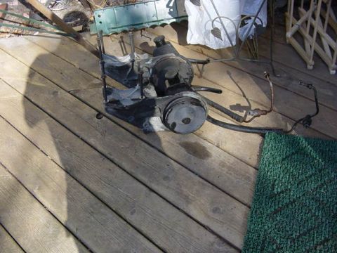 1992 Ford Bronco - Removed radiator and engine fan/pulley assembly with attached hoses resting on a wood deck near patio furniture.