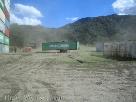 1990 Ford Bronco - lone green Evergreen shipping container sits in a dusty open yard surrounded by hills, with equipment off to the sides.
