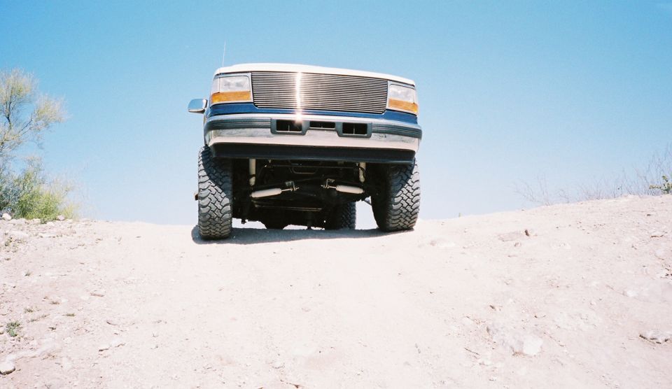 Blue and white Ford Bronco with aftermarket grille and large tires, viewed from the front