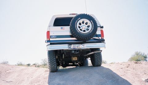 1996 Ford Bronco - Rear view of a 1996 Ford Bronco with a spare tire on the tailgate, on an off-road trail.