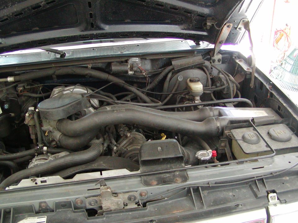 Engine bay of a 1988 Ford Bronco showing air cleaner, hoses, battery, and radiator area