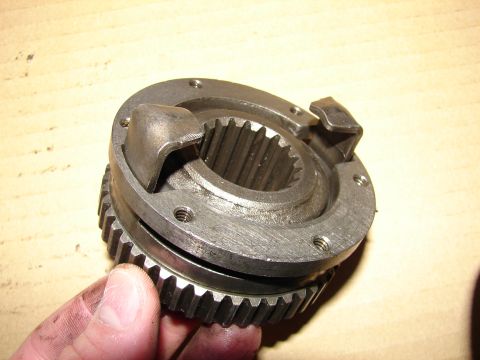 1996 Ford Bronco - A metal hub assembly part with visible gear teeth is held by a hand against a wooden surface.