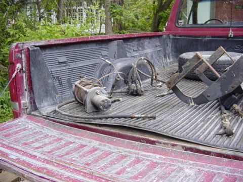 1992 Ford Bronco - Winch and various parts are stored in the bed of a red pickup truck.