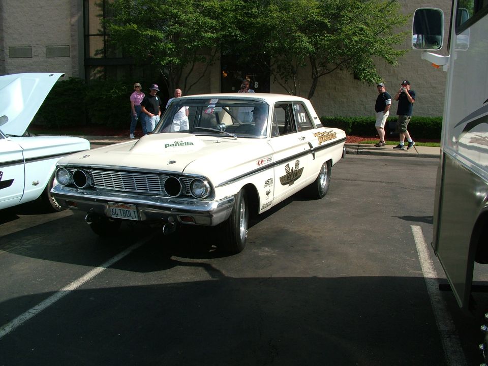 White 1964 Ford Fairlane sedan with racing decals and a hood scoop, parked in a lot