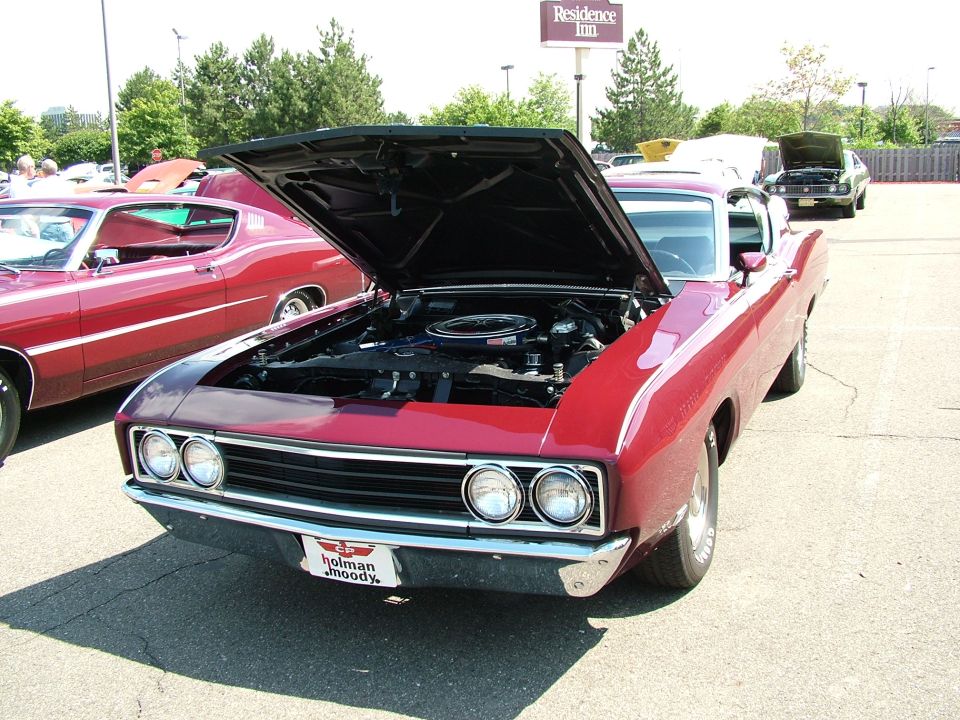 Red 1970 Ford Torino GT parked, hood open showing engine. Another red car is to the left. Residence Inn sign in background