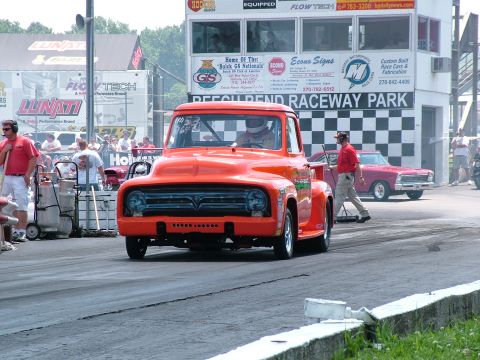 1972 Ford Ranchero - An orange pickup truck, likely a 1956 model, is on the drag strip with another car in the background.