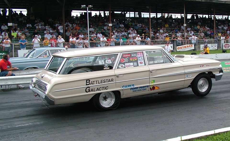 1964 Ford station wagon drag racing with 'Battlestar Galactic' on door, another car in background