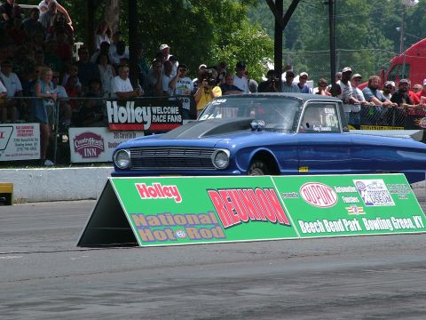 1972 Ford Ranchero - A blue drag car sits at the starting line in front of a crowd and event signage.