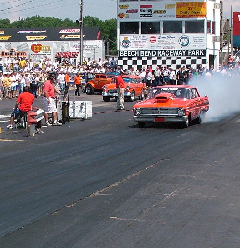 Orange vintage Ford doing a burnout at drag strip starting line