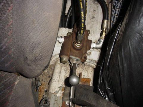 1992 Ford Bronco - A cast-iron hydraulic control valve mounted on a bare cab floor between the seats, plumbed with black high-pressure hose and brass fittings…
