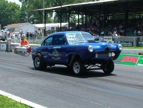 1972 Ford Ranchero - A blue drag car with a prominent supercharger and 'Wild Weasel' graphics races down the track.
