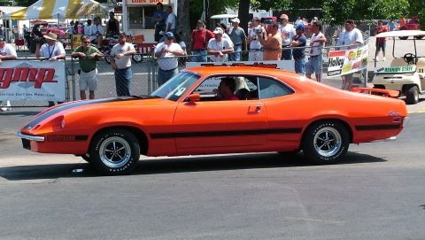 1972 Ford Ranchero - Orange 1972 Ford Ranchero with black stripes on a race track, seen from the side.