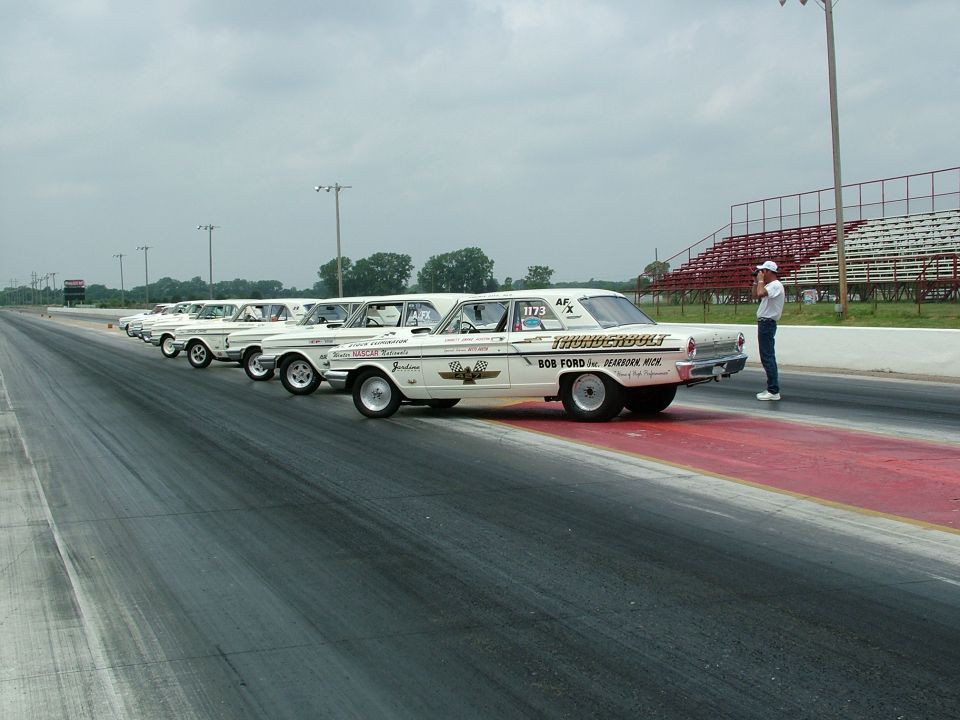 White 1964 Ford Thunderbolt drag car with 'Thunderbolt' text on rear quarter panel, parked on a drag strip