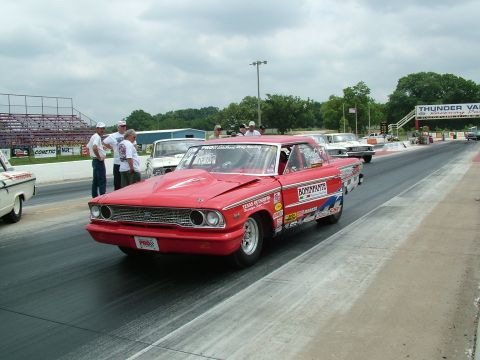 1972 Ford Ranchero - A red 1964 Ford Falcon drag car is on the track with other vehicles and spectators in the background.
