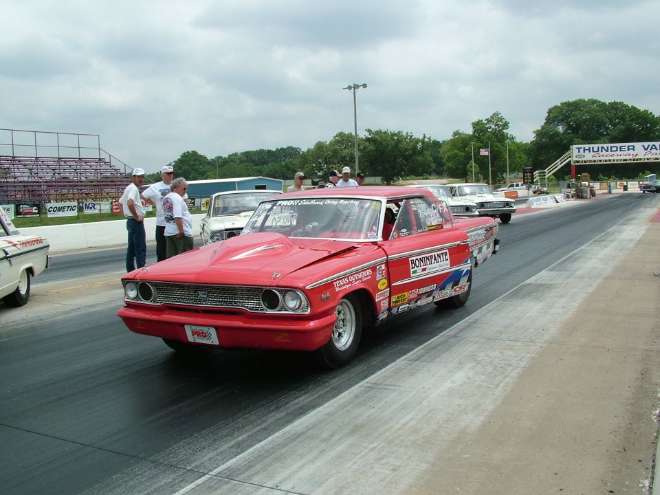 Red 1964 Ford Falcon drag car with hood scoop and racing decals on a drag strip