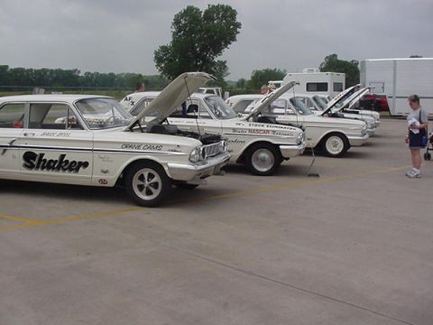 1972 Ford Ranchero - A row of classic white race cars are displayed with their hoods open, parked on a paved lot.