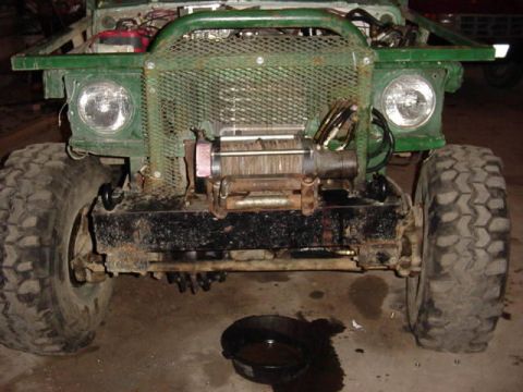 1992 Ford Bronco - Front end of a modified green 4x4 truck showing a recovery winch, expanded-metal grille guard, dual round headlights and oversized mud-terr…