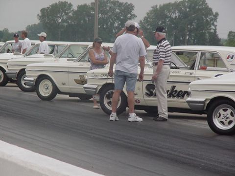 1972 Ford Ranchero - A line of vintage race cars are parked on the track, with spectators milling about.