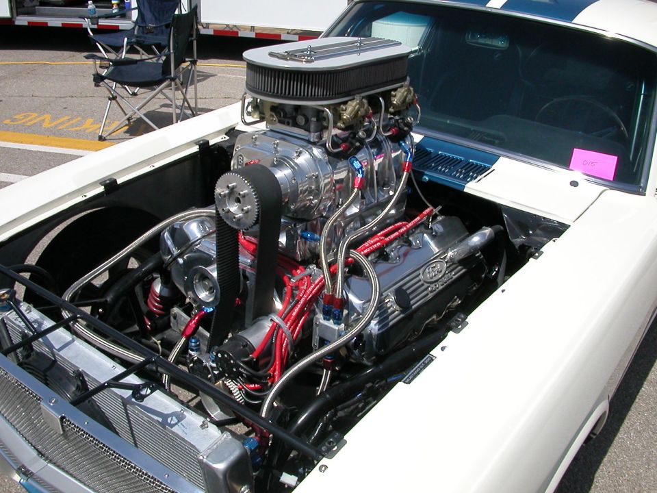 White car's engine bay with a polished supercharger, chrome valve covers, and red spark plug wires
