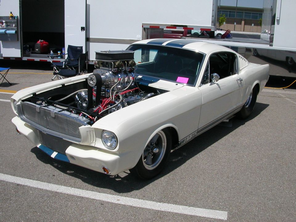White custom 1965 Mustang with exposed supercharged engine and racing stripes
