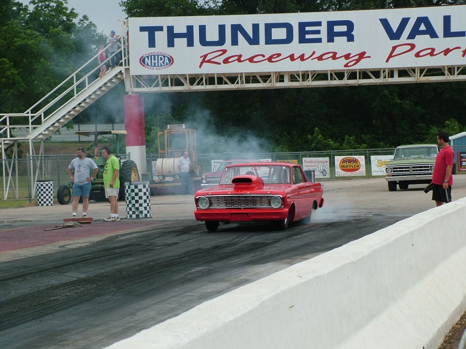 Red drag car with hood scoop on track, emitting smoke