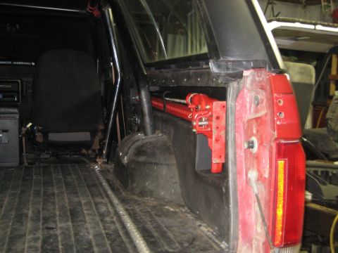 1990 Ford Bronco - A red hi-lift jack is mounted inside the cargo area of a red SUV, alongside the interior paneling and taillight assembly.