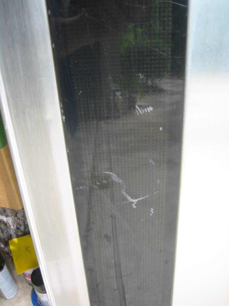 Close-up of a tinted glass panel with white scratches and a metal frame