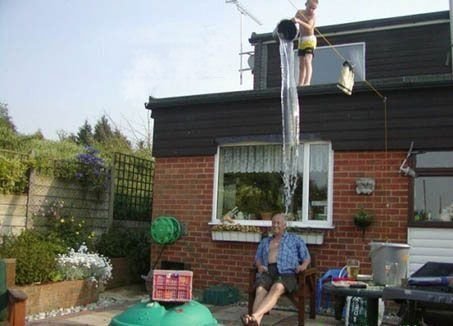 1976 Ford F-150 - A man relaxes in a chair as a large stream of water cascades from a bucket on the roof of a brick house.