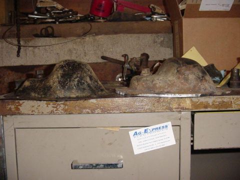 1992 Ford Bronco - Two removed cast differential housings, caked in dried gear oil and grime, sit on a cluttered wooden workbench in a shop. Hand tools, a spr…