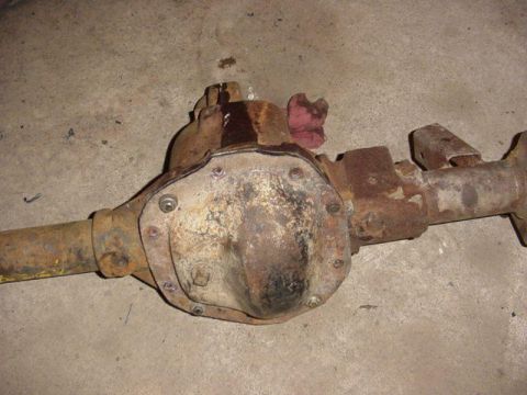 1992 Ford Bronco - A rusty removed solid axle assembly lying on a concrete floor, photographed looking down at the differential cover. The stamped bolt-on cov…
