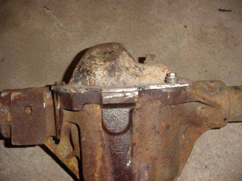 1992 Ford Bronco - A heavily rusted axle center section (differential housing) with a cast pumpkin and bolted cover, resting on a concrete floor. Surface rust…