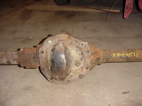 1992 Ford Bronco - A rusty rear axle housing lying on a concrete garage floor, with the bolt-on differential cover installed and heavy surface corrosion acros…