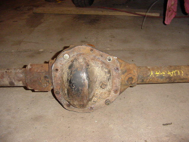 Rusty rear axle housing with differential cover on a concrete garage floor