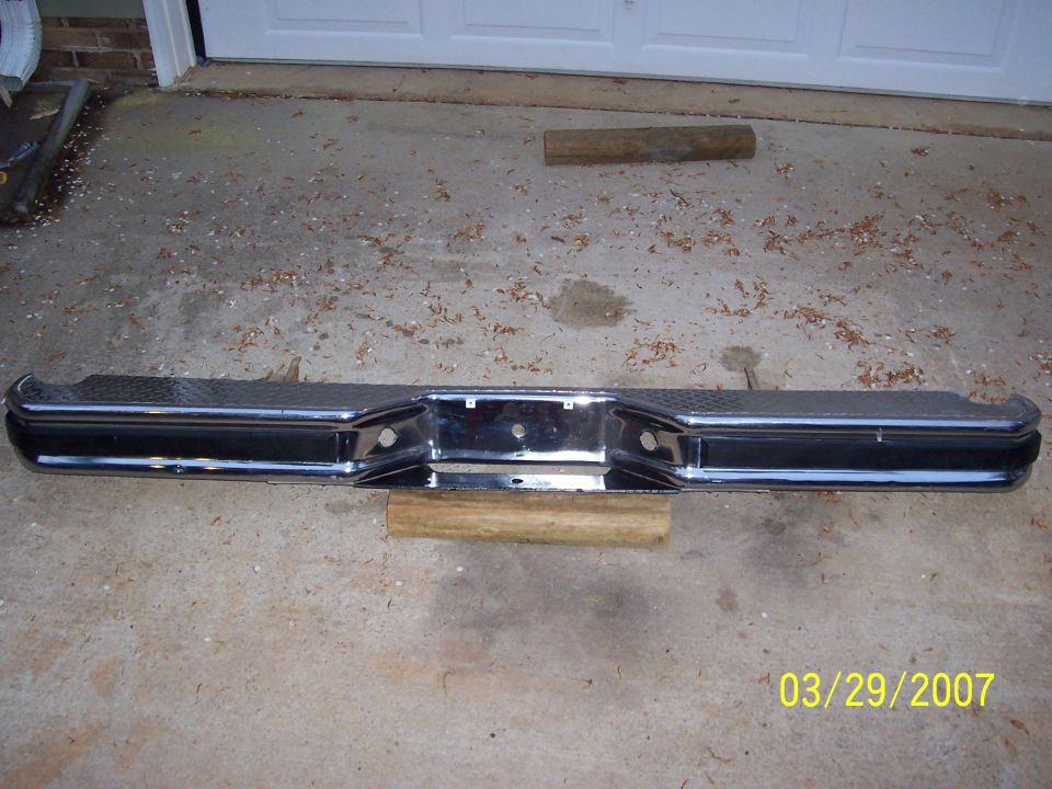 Chrome rear bumper with diamond plate texture, resting on wooden blocks
