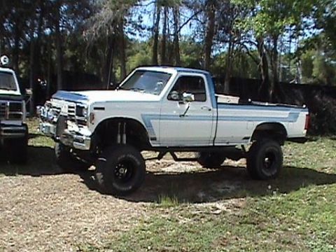 1986 Ford Bronco - This lifted pickup truck has a two-tone paint scheme with blue stripes along the body.