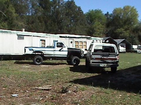 1986 Ford Bronco - A white SUV and a pickup truck are parked in a grassy area next to a mobile home.