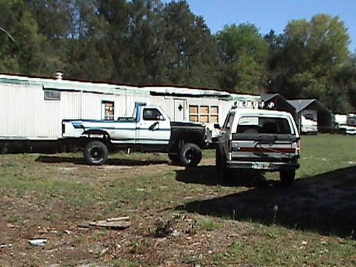Two trucks, one white SUV and one black and white pickup, parked in a yard