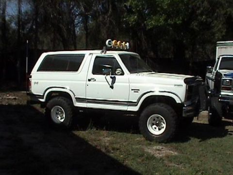 1986 Ford Bronco - A white Ford Bronco with off-road modifications is parked next to another vehicle.