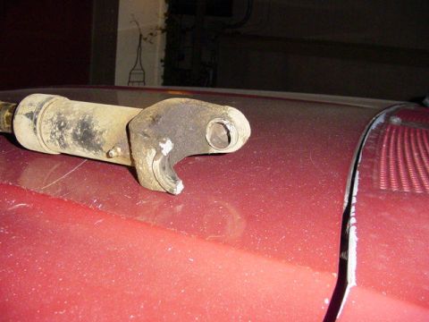 1992 Ford Bronco - A close-up view of a rusty suspension component resting on the red hood of a vehicle.