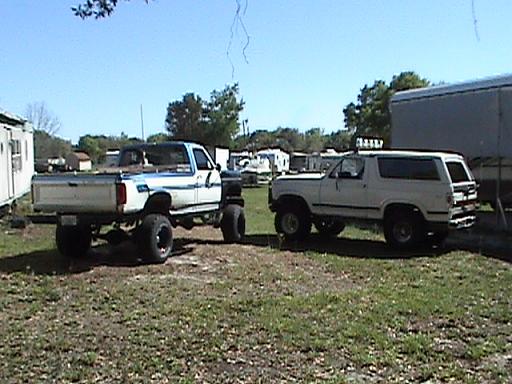 White 1987 Ford Bronco parked next to a lifted pickup truck