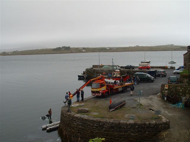 Crane truck loading a boat at a harbor with several other vehicles parked nearby