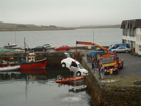 1989 Ford Bronco - A white van is being recovered from the water by a crane, with a tow truck and other vehicles present at the scene.