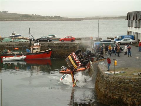 1989 Ford Bronco - A truck has tipped over the edge of a harbor wall, partially submerging a car in the water below.